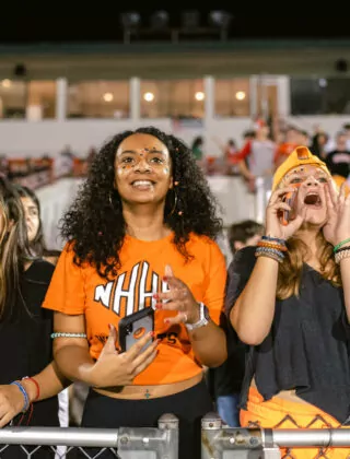 Crowd of high school students cheer on football team.