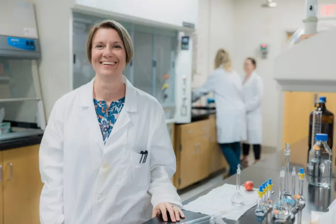 Female pharmaceutical scientist smiles in lab.