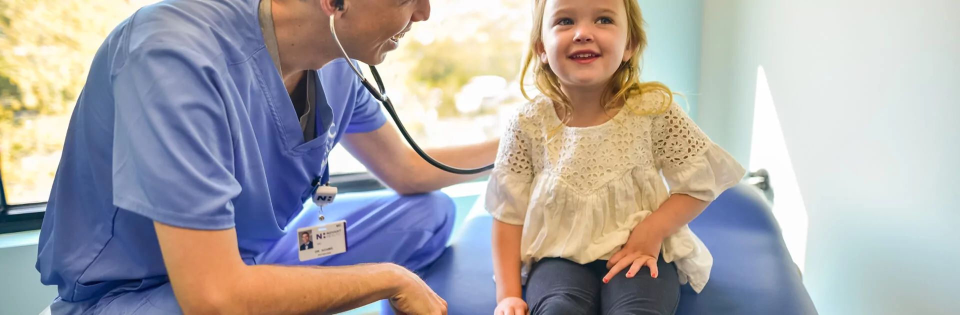 Male doctor listens to smiling child's heartbeat.