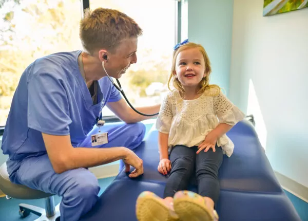 Male doctor listens to smiling child's heartbeat.