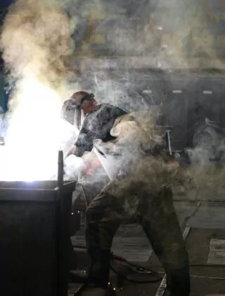 Man wearing welding mask working in a cloud of smoke.