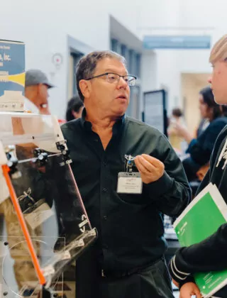 Manufacturing employer speaks with interested student at career fair.