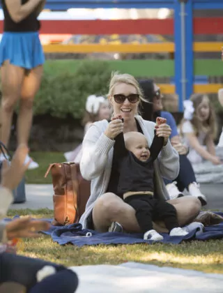 Mother puts baby's hands in the air at outdoor concert in green park.