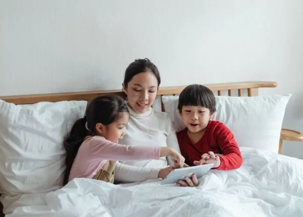 Mother sits in bed with two children playing with tablet.