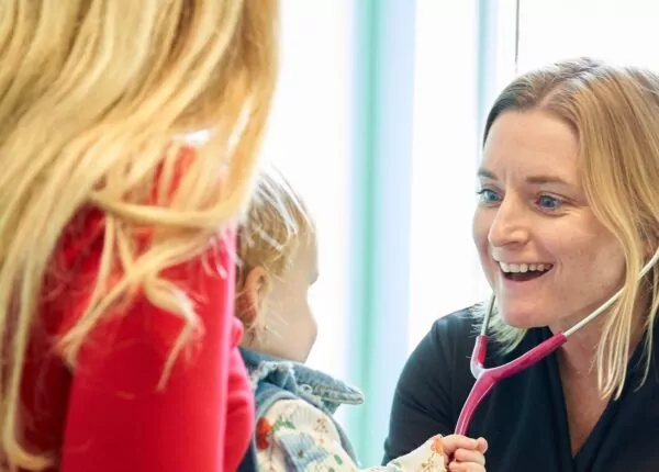 Small child pulls on smiling doctor's stethoscope in doctor's office.