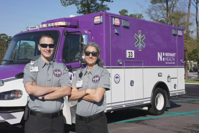 Two EMS crew members stand in front of an ambulance.