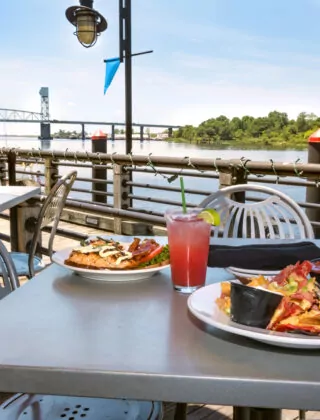 Two plates of food and colorful drinks served at a restaurant outside beside the Cape Fear River.