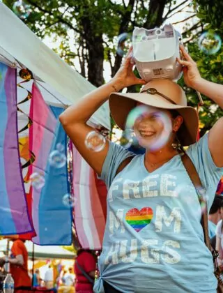 Woman smiling at pride festival with a bubble blower on her head.