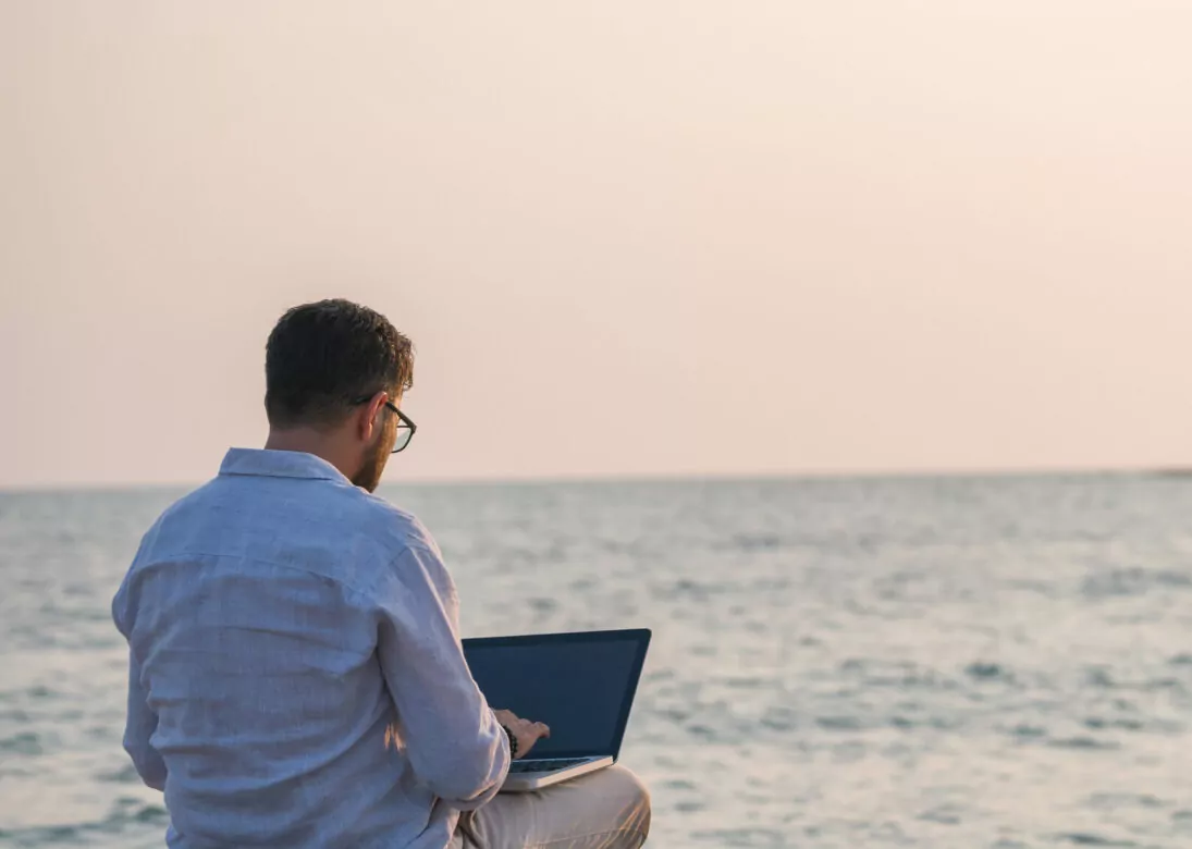 Man sitting on the beach and using his laptop at sunset.